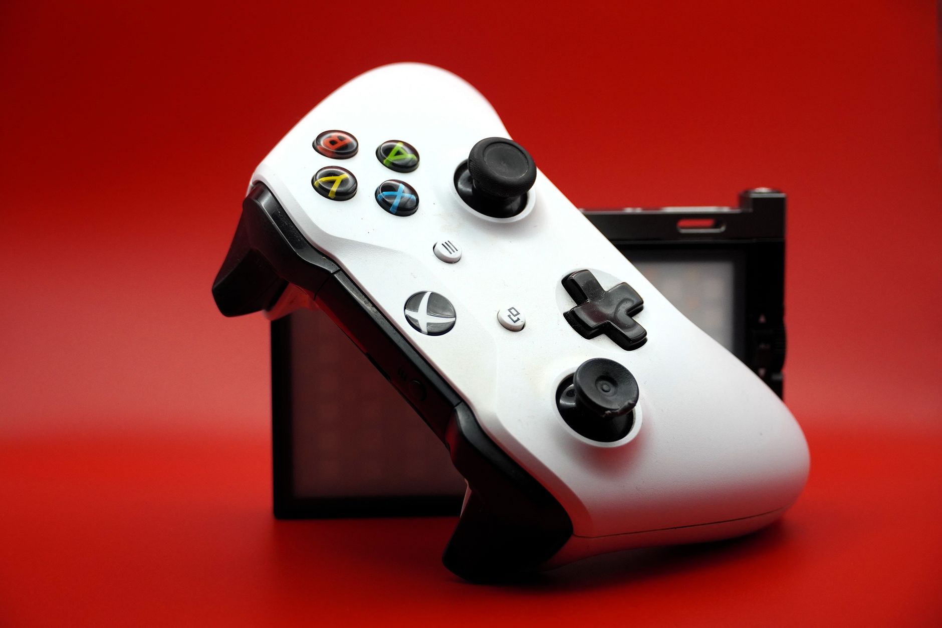 Close-up of a white gaming controller with black buttons against a vivid red backdrop.