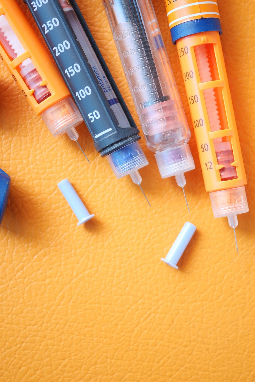 Top view of insulin syringes with caps on a vibrant orange surface.