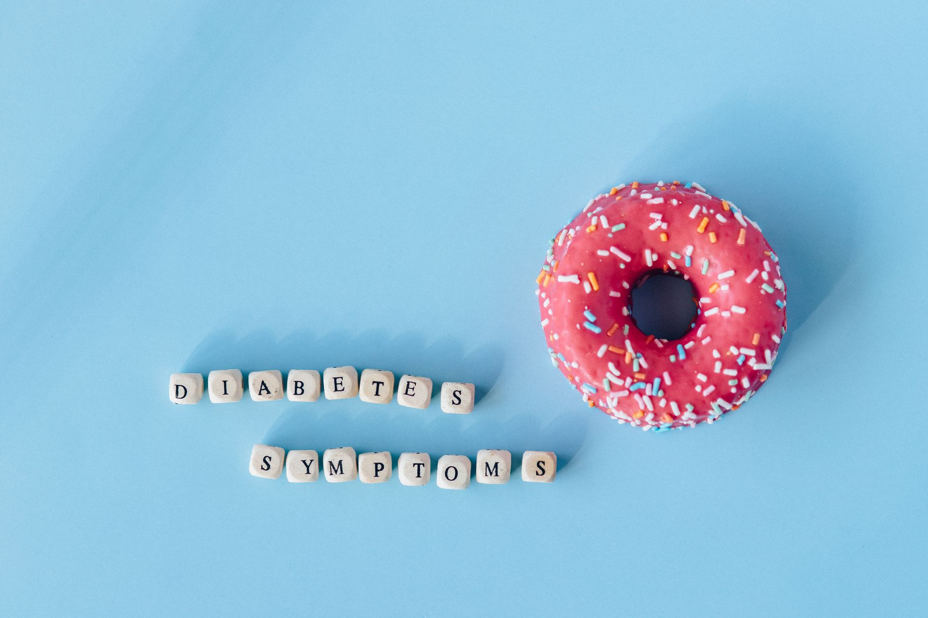 A pink frosted donut with diabetes symptoms text on a blue background, highlighting awareness.