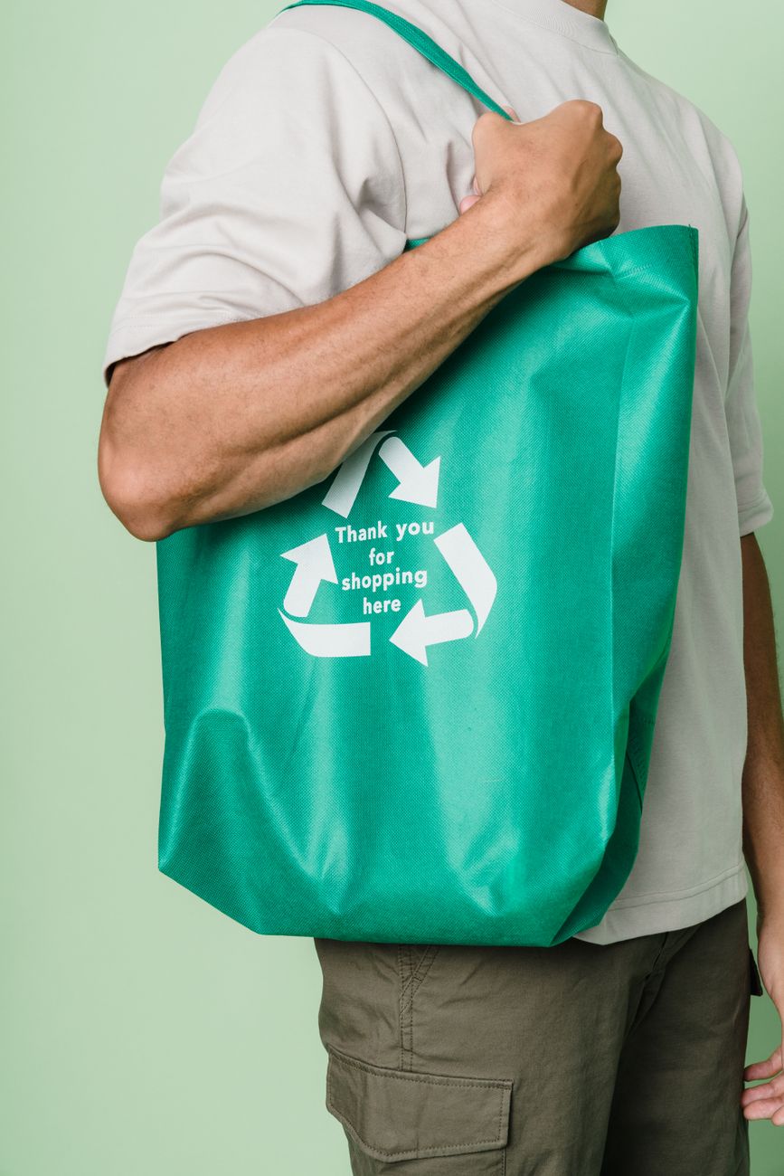 Close-up of an adult holding a green recycling symbol tote bag indoors.