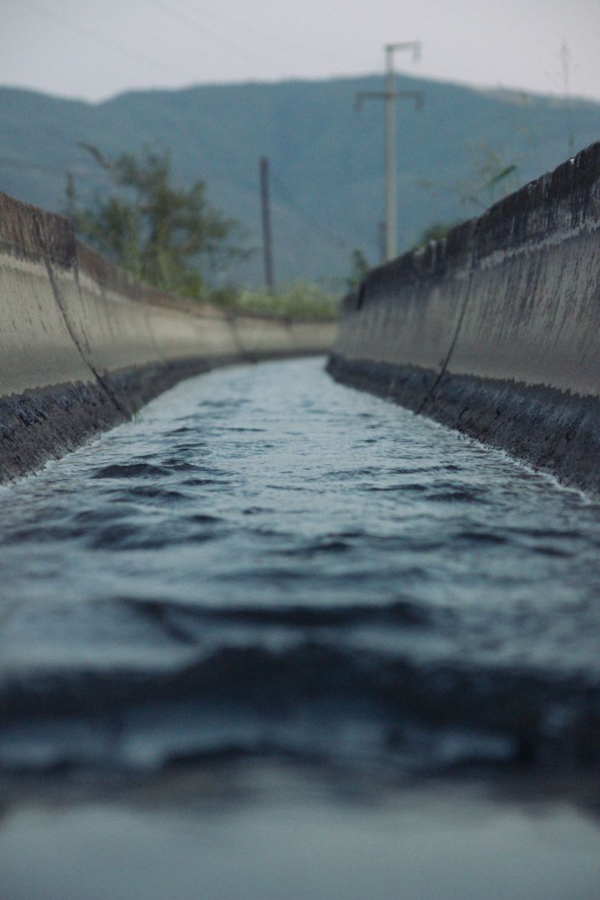 Close-up shot of water flowing through a concrete channel with mountains in the background.