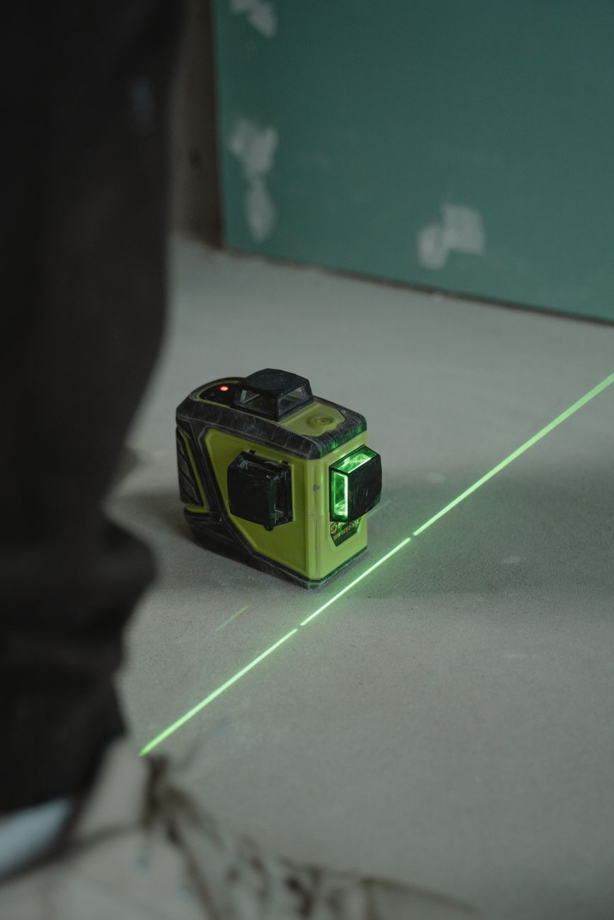 Close-up of a green line laser level used for precise measurements on a construction site floor.