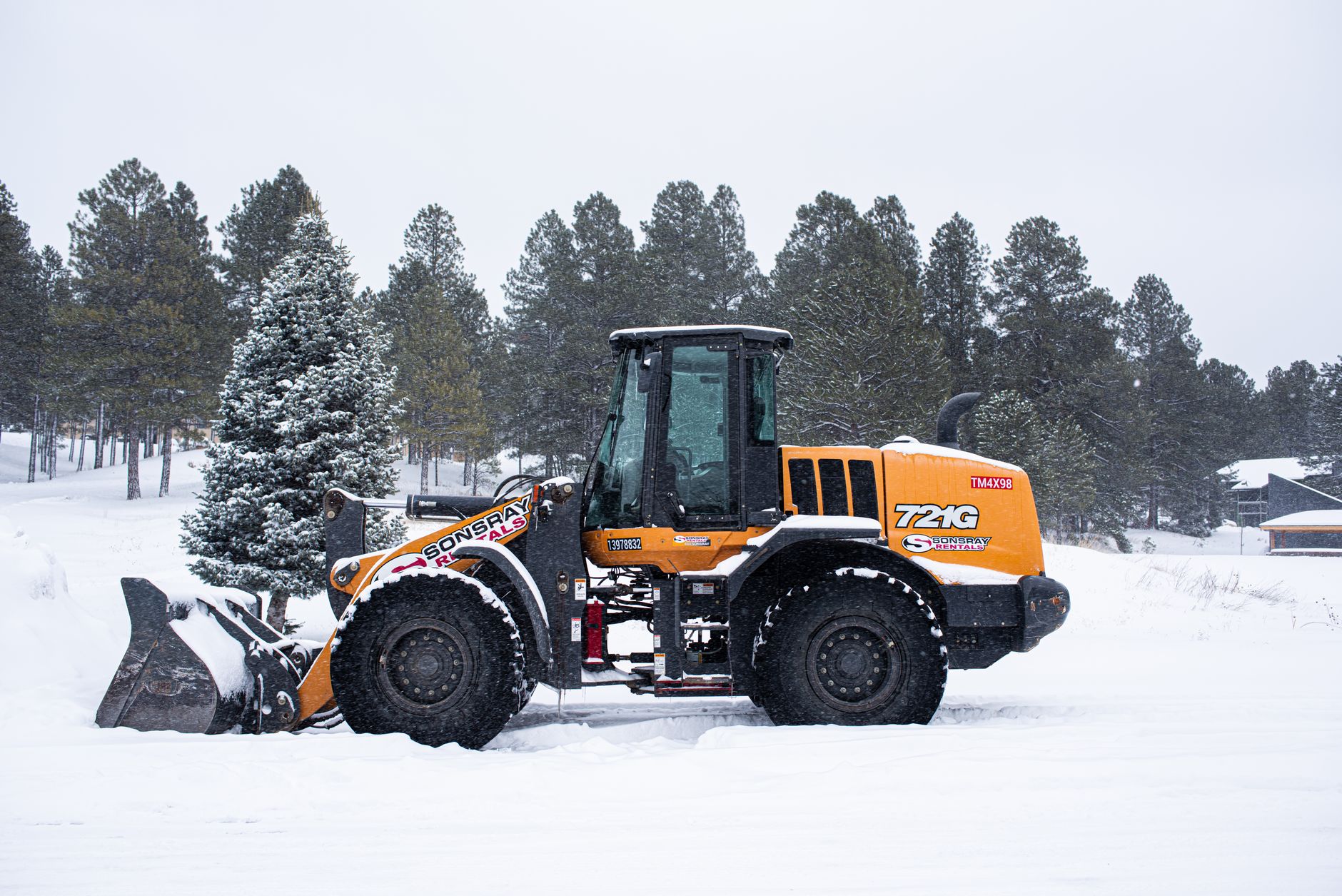 A yellow wheel loader in a snow-covered forest clearing during winter.