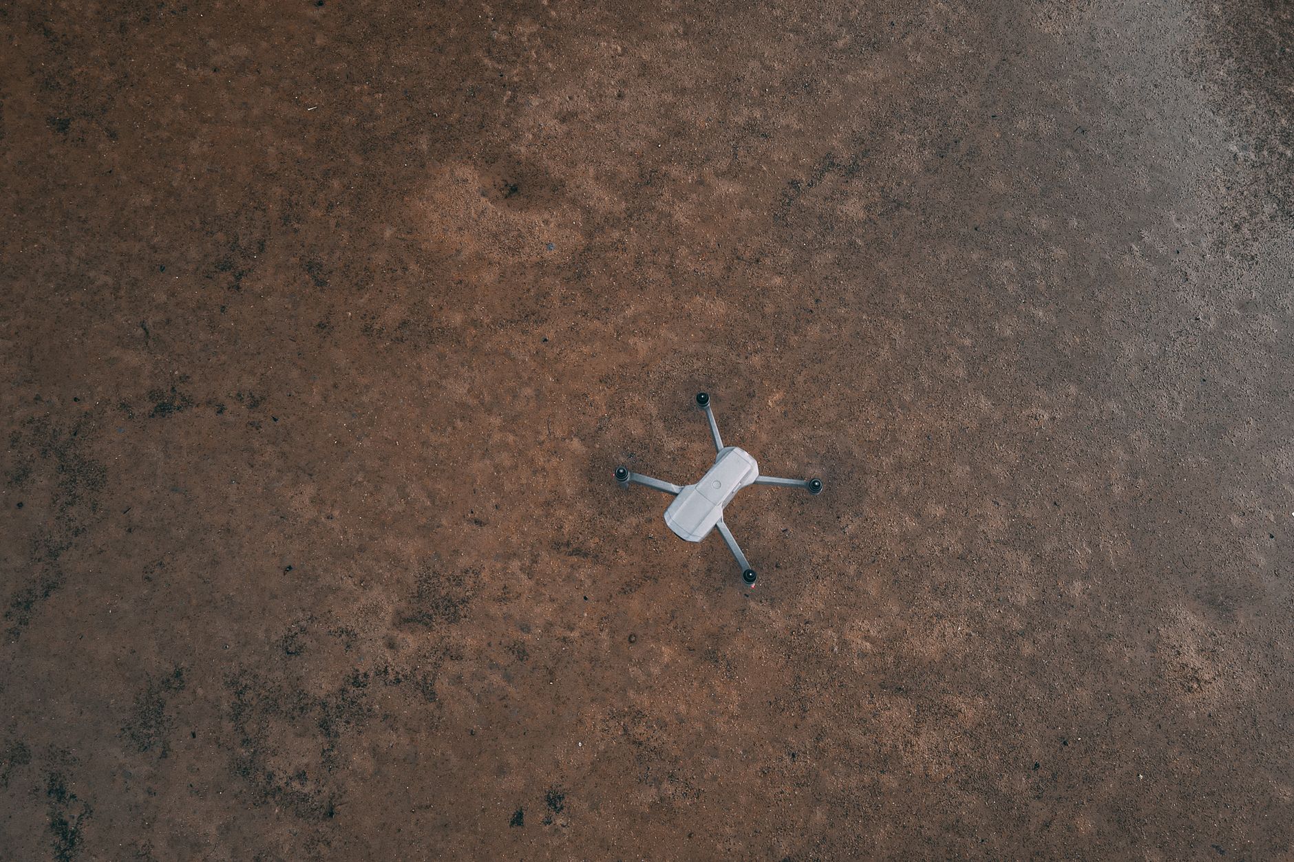 A single drone rests on a textured, earthy surface, captured from above.